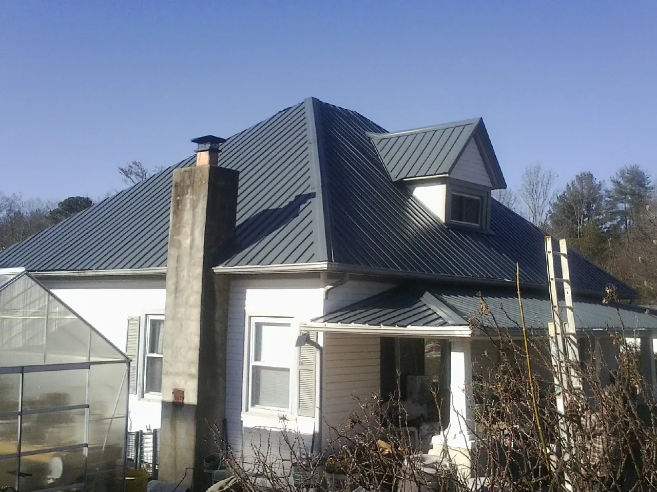 Dark blue standing seam metal roof on a white farmhouse with dormer — Slate & Tile Roof Repair by Roofing Brothers in Flushing