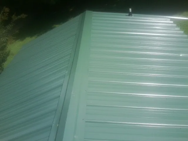 New green metal panels meeting at the ridge of a roof — Flat Roof Repair work by our crew in Flushing