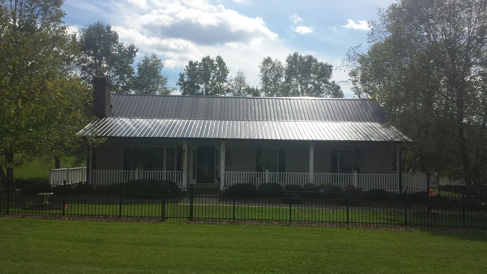 Gray metal roof on a brick ranch with a full width front porch — Gutter Guard Installation work by our crew in Flushing